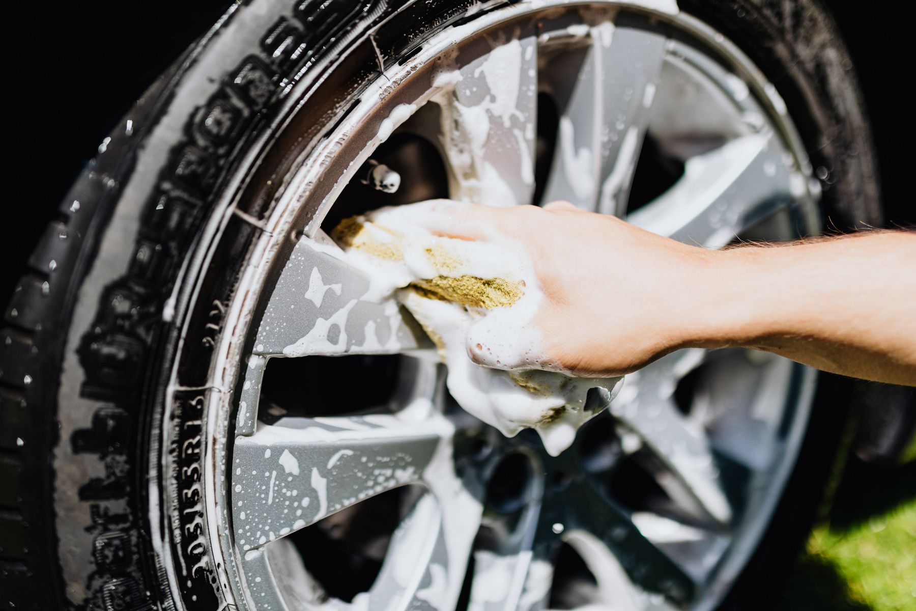 A hand carefully cleaning a wheel covered with soap suds